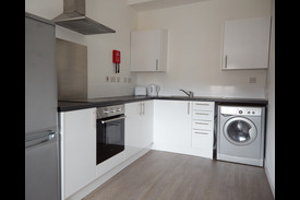 photograph of a kitchen with cupboards, oven and hobs, fridge, sink, and washing machine.